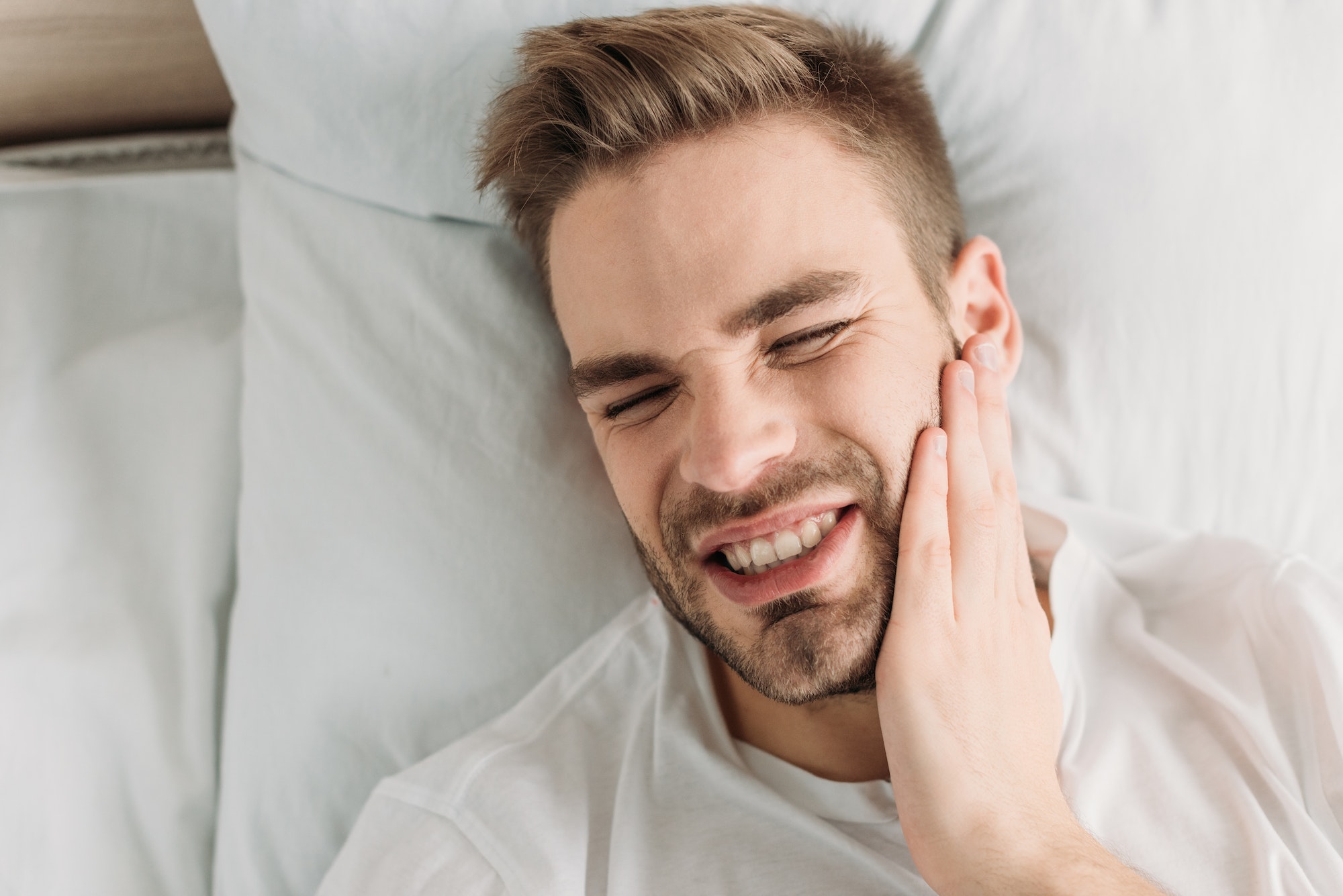 top view of young man touching cheek while suffering from toothache